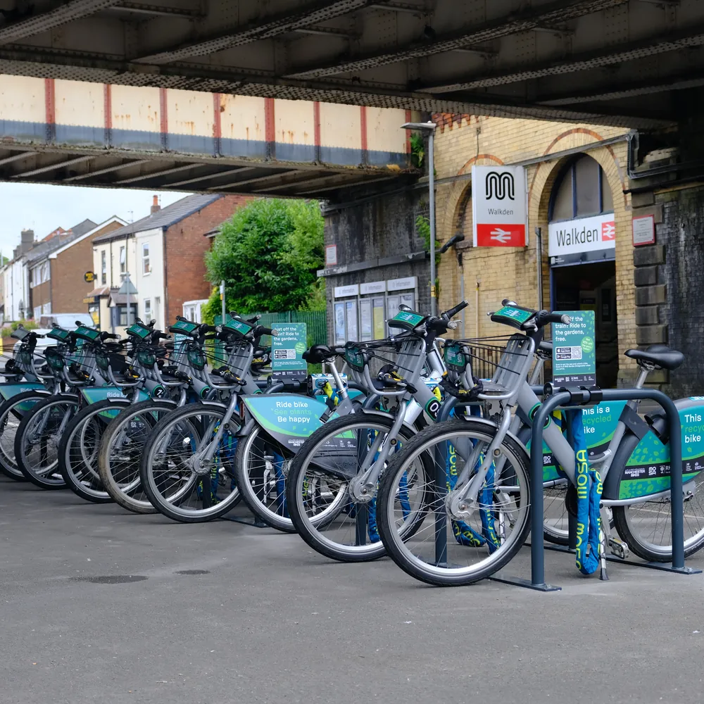 Shared bikes docked in a row outside Walkden station, under the railway bridge.
