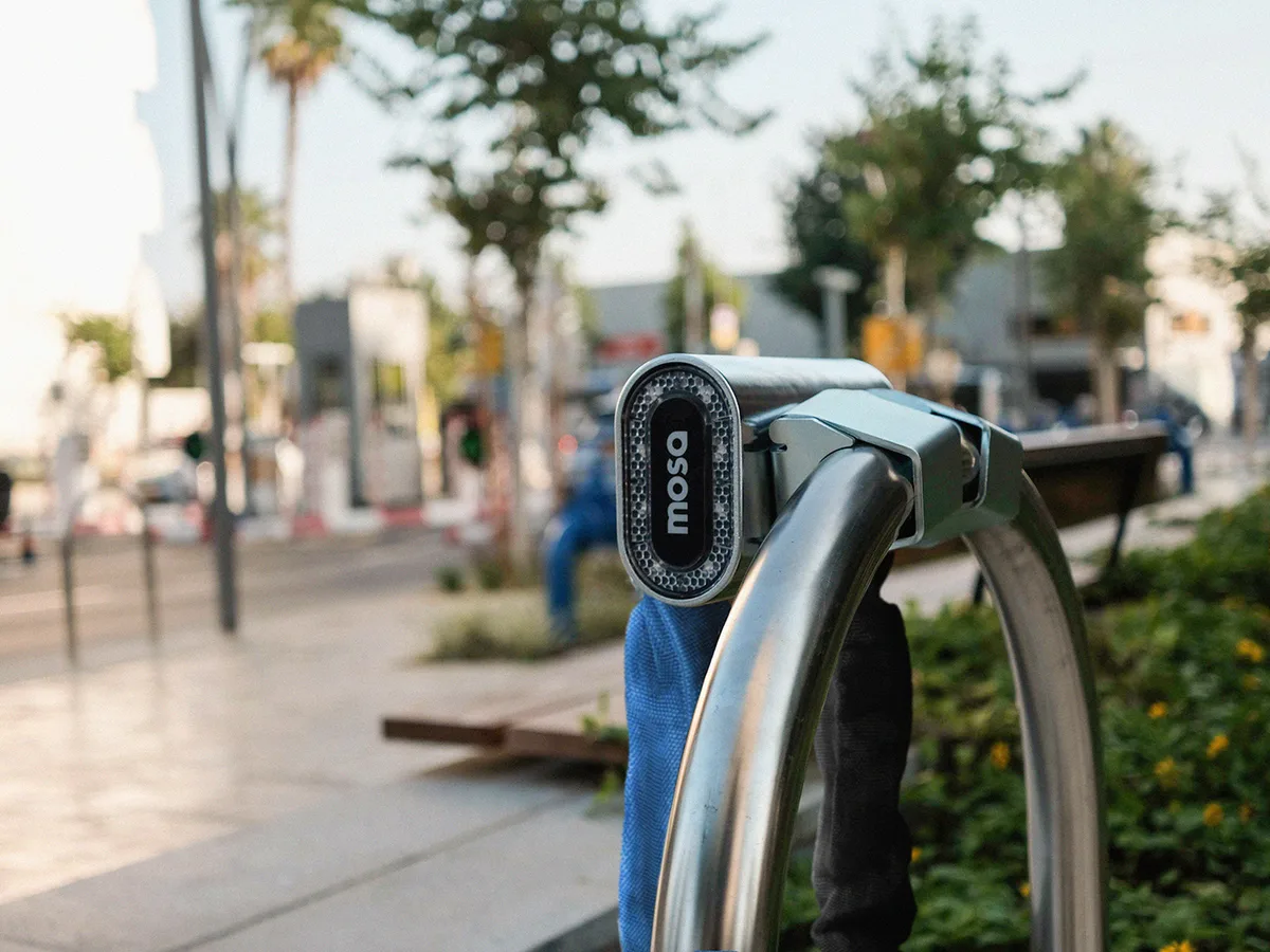 A Mosa smart dock fitted to a steel cycle rack on a tree-lined Tel Aviv street.