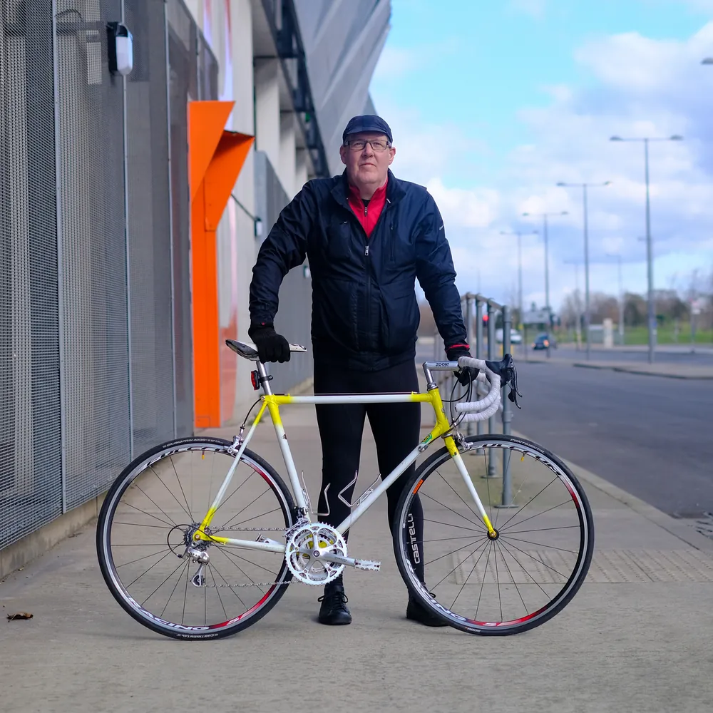 A rider standing beside their own yellow and white road bike.